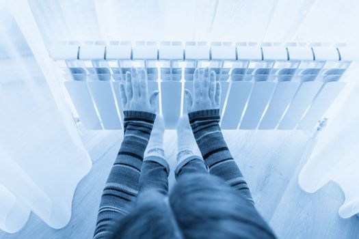 Girl warms up the frozen hands above hot radiator, close up