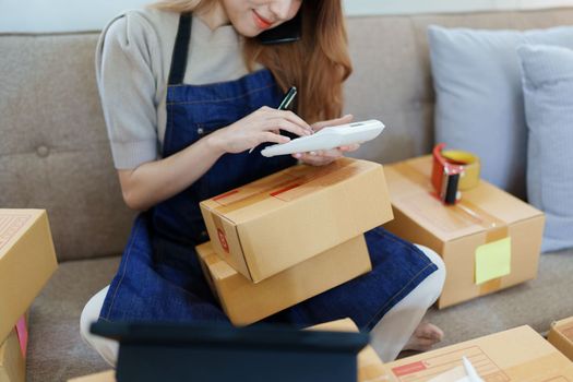 Starting small business entrepreneur of independent Asian woman smiling using computer laptop with cheerful success of online marketing package box items and SME delivery concept.