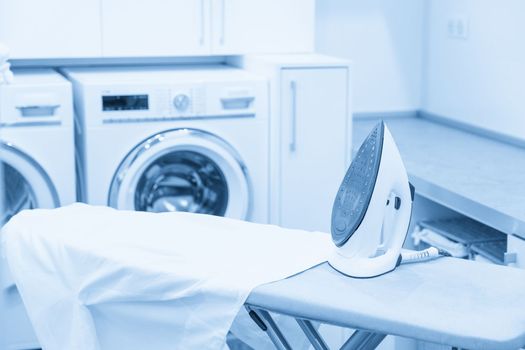 Iron on ironing board with white shirt in modern laundry room