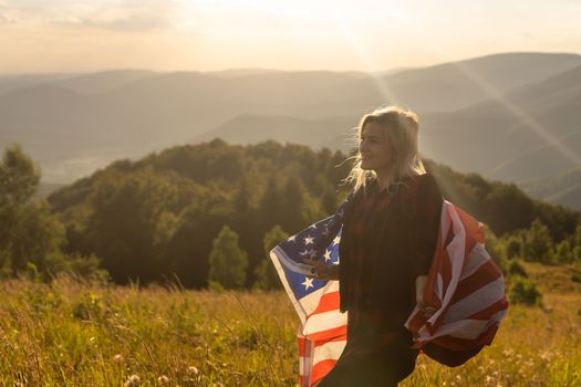 Young woman holding American flag on sky background.