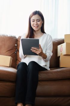 Starting small business entrepreneur of independent young Asian woman online seller is using tablet computer and taking orders to pack products for delivery to customers. SME delivery concept.