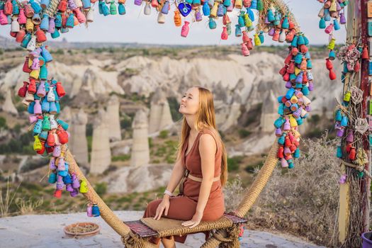 Young woman exploring valley with rock formations and fairy caves near Goreme in Cappadocia Turkey. Wish tree. Small multi-colored jugs with inscriptions, wishes hanging on the branches of a tree., against the backdrop of sand ruins and blue sky.