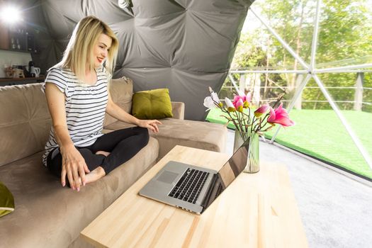 Happy young woman chatting online by using laptop in dome camping. Glamping vacation concept.