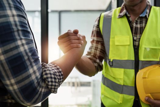 Architect and engineer construction workers shaking hands after finish an agreement in the office construction site, success collaboration concept.