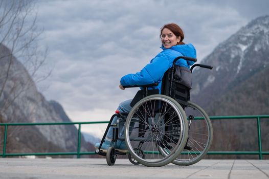 A woman in a wheelchair on a point view admires the high mountains. Thrust to life