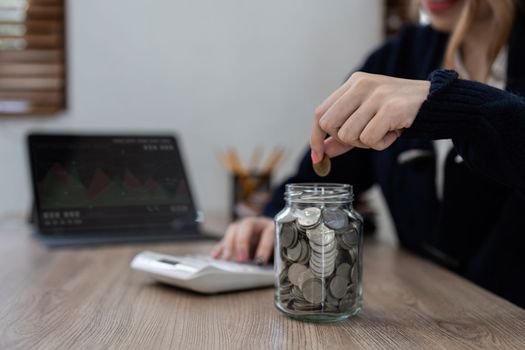 Businesswoman hands carrying a coin put to the saving pocket for her savings idea, calculator, and account.