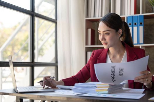 Asian Businesswoman Using laptop computer and working at office with calculator document on desk, doing planning analyzing the financial report, business plan investment, finance analysis concept...