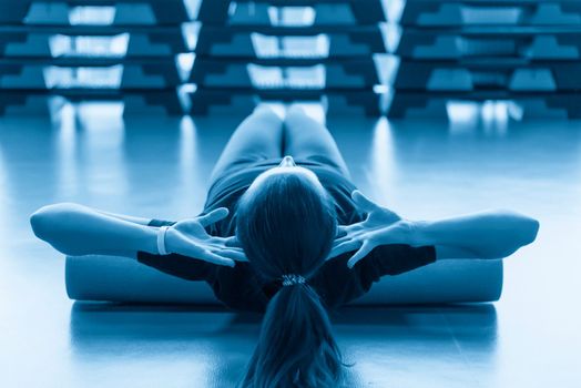 Attractive female doing foam roller exercise and posing in modern bright fitness center. Toned image.