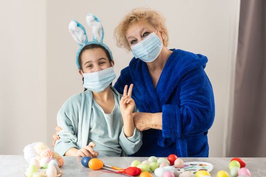 grandmother and children are painting eggs. Happy family are preparing for Easter. Cute little girls wearing bunny ears
