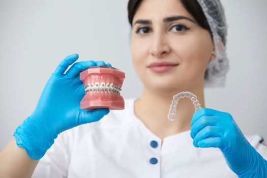 Doctor orthodontist showing model of human jaw with wire braces and aligners explaining difference