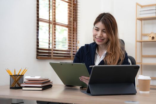 Asian woman Using laptop computer and working at office with calculator document on desk, doing planning analyzing the financial report, business plan investment