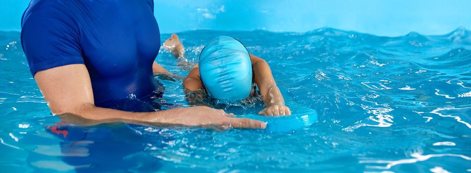 Male trainer teaching boy how to swim in indoor pool with pool flutter board