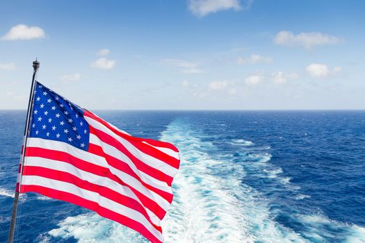 USA national flag on cruise ship with wake or trail on ocean surface on background