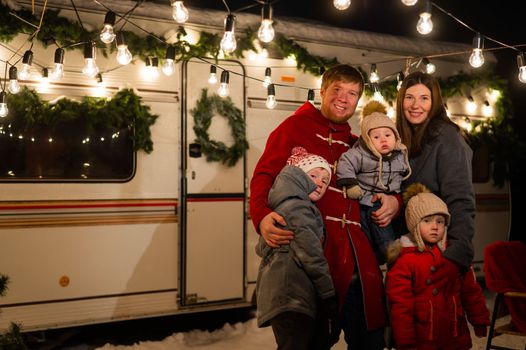 Happy caucasian family hugging outdoors. Christmas decorations. Parents and three sons travel in a camper