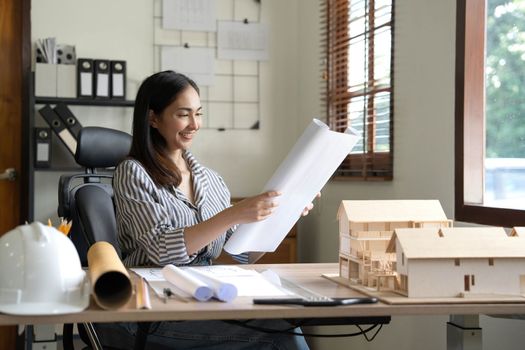 Architecture, building, construction and real estate concept - Happy smiling female architect with blueprint, ruler and living house model on table working at home office. Architect woman