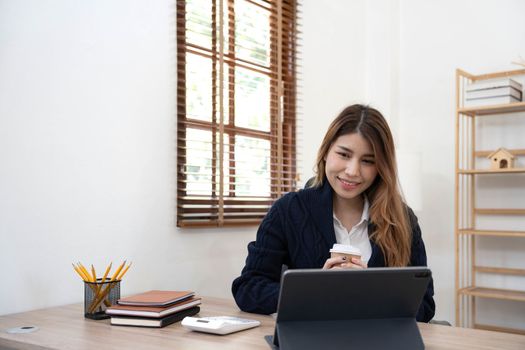 Asian woman Using laptop computer and working at office with calculator document on desk, doing planning analyzing the financial report, business plan investment