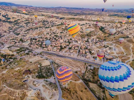 Colorful hot air balloons flying over at fairy chimneys valley in Nevsehir, Goreme, Cappadocia Turkey. Spectacular panoramic drone view of the underground city and ballooning tourism. High quality.