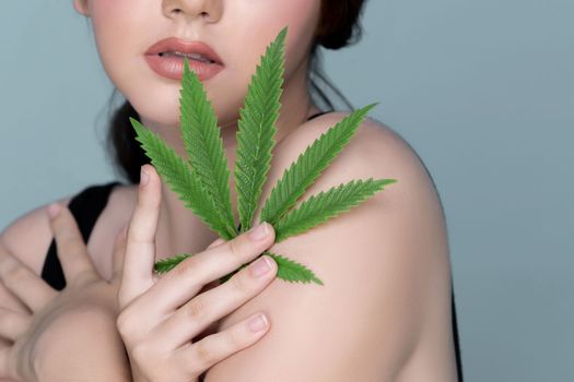 Closeup portrait of charming girl with fresh skin holding green leaf for beauty skin care made from cannabis leaf. Cosmetology and cannabis concept with isolated background.