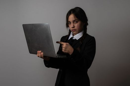 A girl with braids in a gothic style on a dark background with laptop.