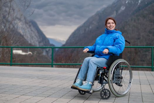 A woman in a wheelchair on a point view admires the high mountains. Thrust to life