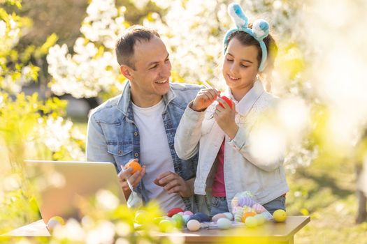 father and daughter coloring easter eggs with laptop in the garden.