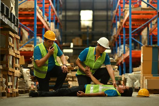 Injured storehouse worker lying unconscious on the concrete floor after fall and being rescued by his colleague.