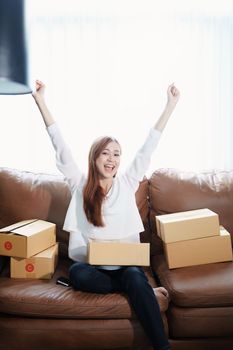 Starting small business entrepreneur of independent Asian woman smiling using computer laptop with cheerful success of online marketing package box items and SME delivery concept.