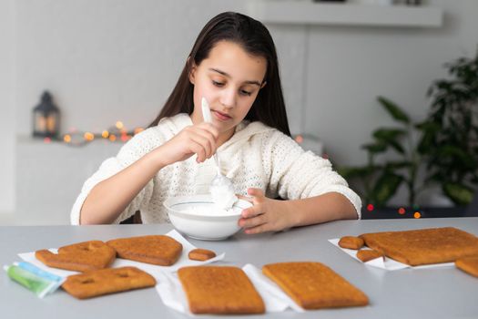 Kids baking Christmas gingerbread house. Children celebrating winter holiday at home. Decorated living room with fireplace and tree. Family activity. Little girl making cookies.