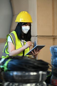 Image of female manager in yellow vest tracking supply order details on digital tablet. Logistic industry concept.