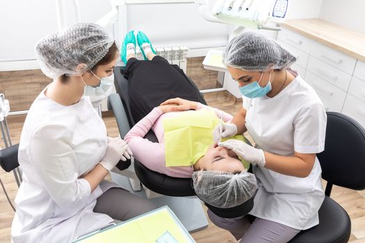 Professional dentist surgeon and assistant performing dental operation in a clinic with modern equipment