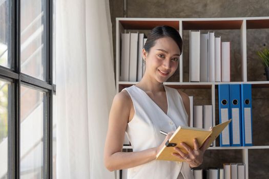 Charming young Asian businesswoman with a smile standing holding documents at the office