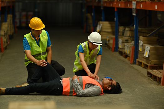 Male supervisor lying unconscious on the concrete floor and colleagues helping and giving the injured first aid.