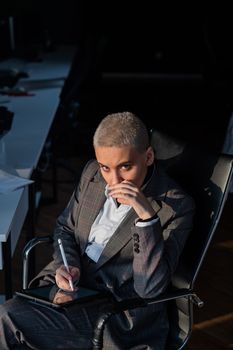 Business woman with short hair sits by the window and writes on a digital tablet with a stylus pen.