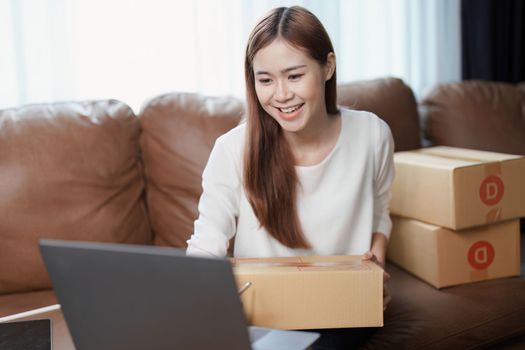 Starting small business entrepreneur of independent young Asian woman online seller is using computer and taking orders to pack products for delivery to customers. SME delivery concept.