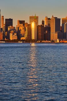 Image of Beautiful southern Manhattan New York City from ferry with golden beam of sunlight reflecting on waters and building