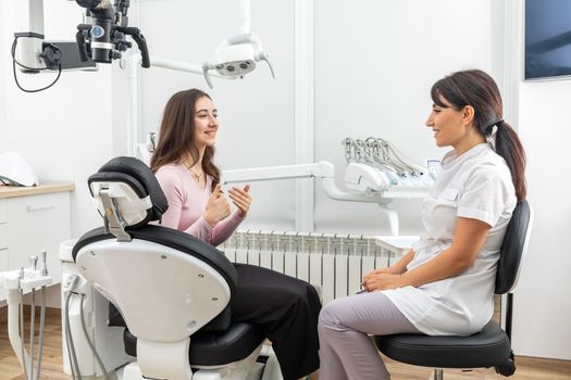 Female dentist talking to a patient during appointment in modern dental clinic before teeth treatment