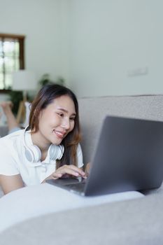 asian teenage girl using computer and wearing headphones at sofa.