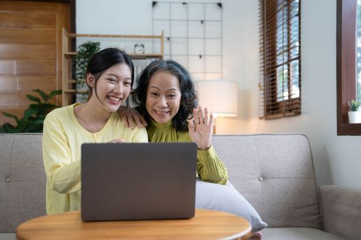 Happy adult granddaughter and senior grandmother having fun enjoying talk sit on sofa in modern living room, smiling old mother hugging young grown daughter bonding chatting relaxing at home together.