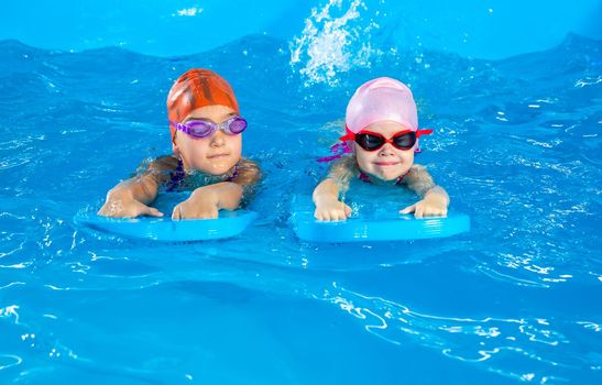 Two little girls having fun in pool learning how to swim using flutterboards