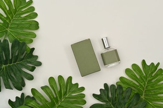  Square fragrance bottle with blank packaging box and tropical leaves on white background.