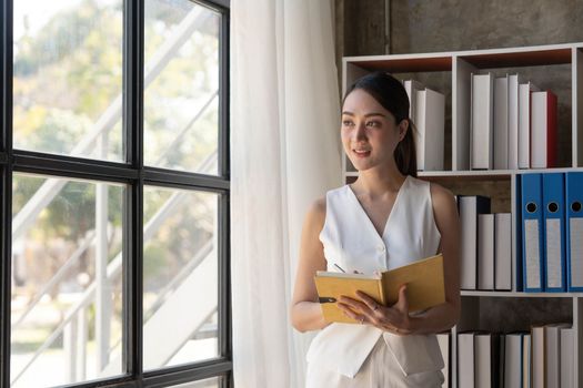 Charming young Asian businesswoman with a smile standing holding documents at the office