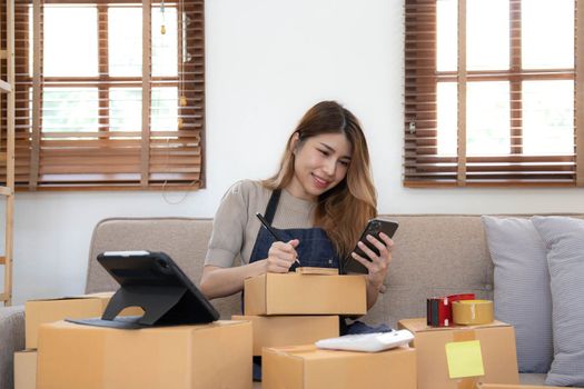 Startup SME small business entrepreneur woman using phone call receive from customer checking product on stock at home office, online marketing packaging delivery box