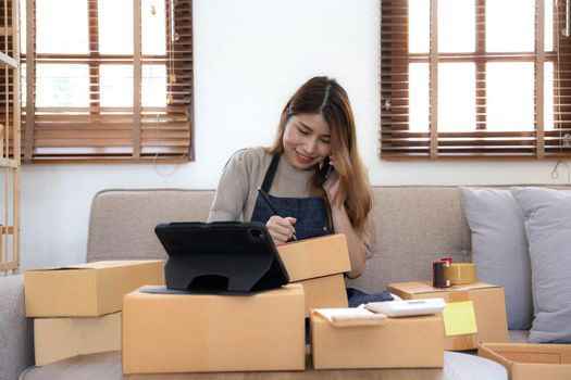 Startup SME small business entrepreneur woman using phone call receive from customer checking product on stock at home office, online marketing packaging delivery box