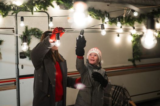 Caucasian woman and son celebrate Christmas in a camper. The boy's mother decorates the van with Christmas lights