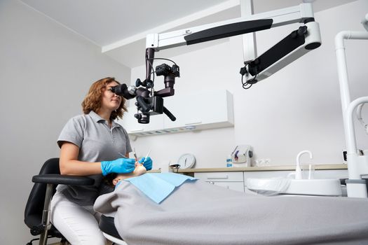 Female dentist with dental tools and microscope treating patient teeth at dental clinic office. Medicine, dentistry and health care concept. Dental equipment