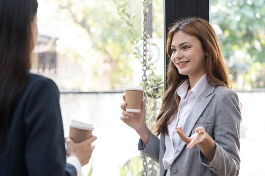 Happy two young Asian business woman holding coffee cup in coworking office..