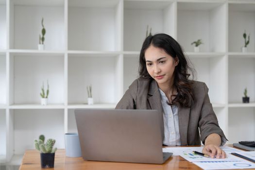 Portrait of serious young businesswoman accountant in formal wear sitting at her work place and use laptop, summarizing taxes, planning future investments, accounting at office...