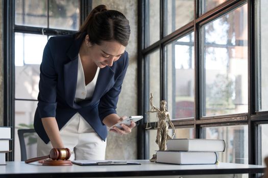 Attractive young lawyer or Businesswoman talking on phone and lawyers discussing contract papers with brass scale on wooden desk in office. Law, legal services, advice, Justice and real estate concept..