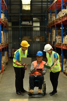 Two young storehouse worker and male manager in wheelchair working on a digital tablet during an inventory check.
