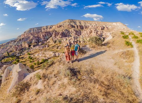 Happy family mother, father and son tourists exploring valley with rock formations and fairy caves near Goreme in Cappadocia Turkey.